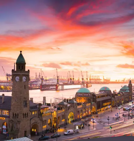 Hamburger Landungsbrücken bei Sonnenuntergang mit Blick auf den Hafen und Kräne im Hintergrund