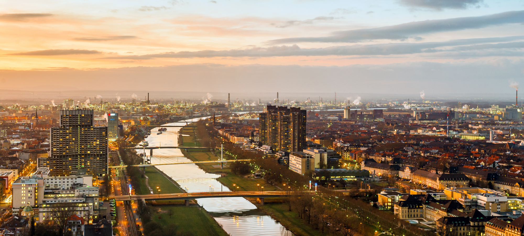Stadtansicht von Mannheim bei Sonnenuntergang mit Rhein und Industrieanlagen